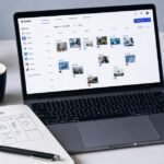 A modern desk showing a laptop with the Buffer social media scheduling dashboard open, a smartphone displaying an Instagram feed, a handwritten weekly content plan notebook, and a cup of coffee