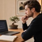 A focused entrepreneur at a minimal desk reviewing a ChatGPT conversation on a laptop, with an open notebook beside them